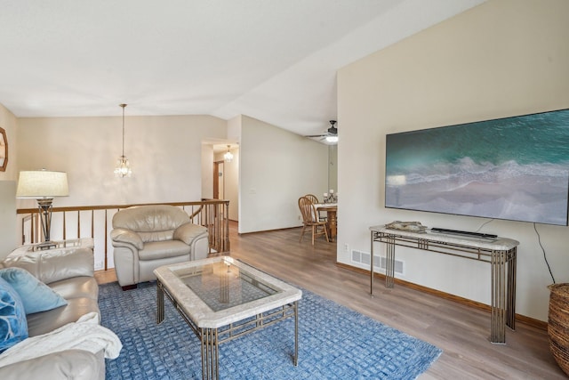living room with vaulted ceiling, wood finished floors, ceiling fan with notable chandelier, baseboards, and visible vents