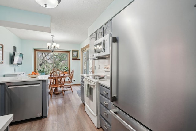 kitchen with light countertops, wood finished floors, a notable chandelier, and appliances with stainless steel finishes