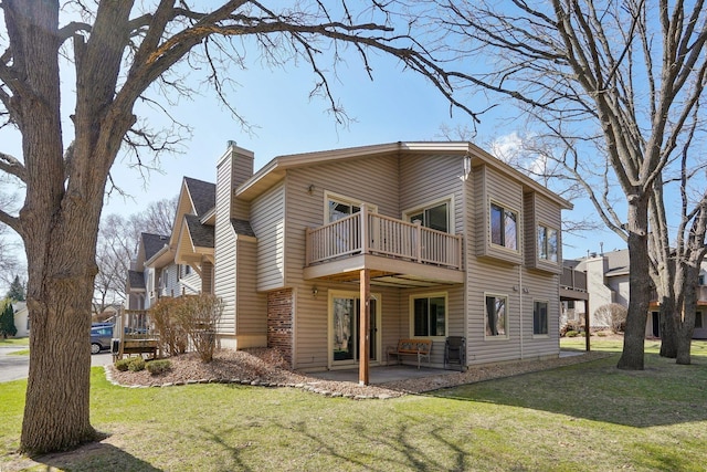 back of property featuring a lawn, a patio area, a chimney, and a balcony