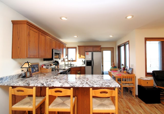 kitchen featuring sink, a kitchen bar, light stone counters, kitchen peninsula, and stainless steel appliances