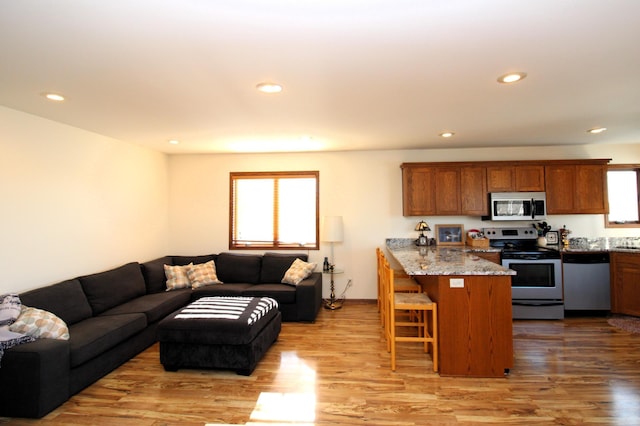 kitchen with light stone countertops, appliances with stainless steel finishes, a breakfast bar area, and light hardwood / wood-style floors