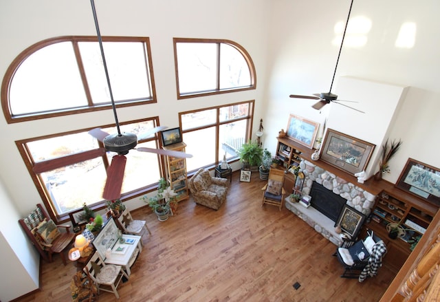 living room with a towering ceiling, a fireplace, hardwood / wood-style flooring, a baseboard heating unit, and ceiling fan