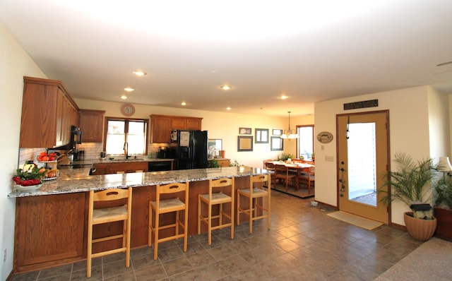 kitchen featuring pendant lighting, sink, black appliances, light stone countertops, and decorative backsplash