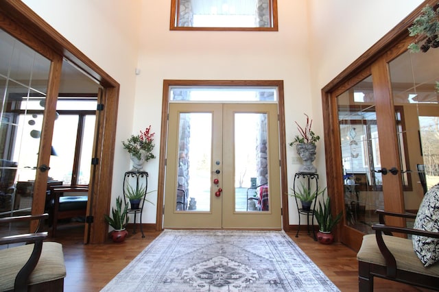 foyer with wood finished floors, french doors, baseboards, and a towering ceiling