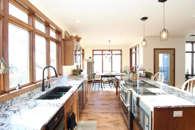 kitchen with brown cabinets, a sink, stainless steel appliances, light wood finished floors, and hanging light fixtures