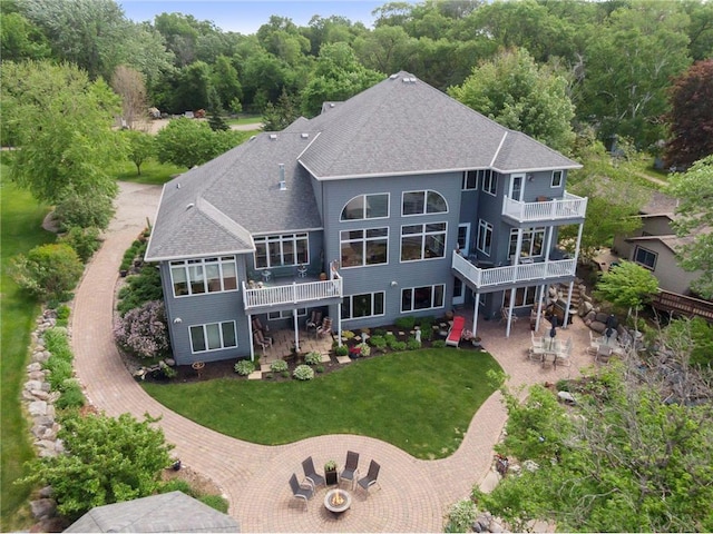 rear view of property featuring a patio area, a lawn, a balcony, and roof with shingles