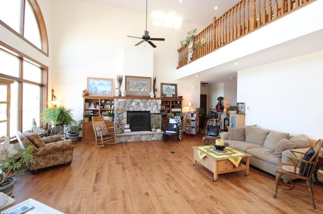 living room with a stone fireplace, wood finished floors, a high ceiling, and ceiling fan