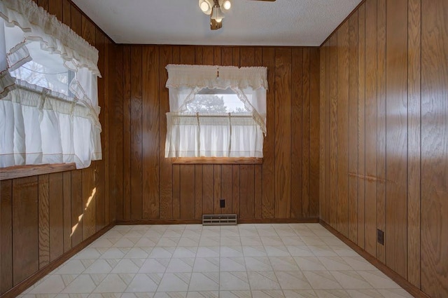 spare room with ceiling fan, plenty of natural light, and wood walls