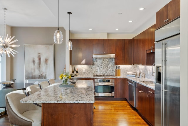 kitchen with decorative light fixtures, a breakfast bar area, backsplash, stainless steel appliances, and light hardwood / wood-style flooring