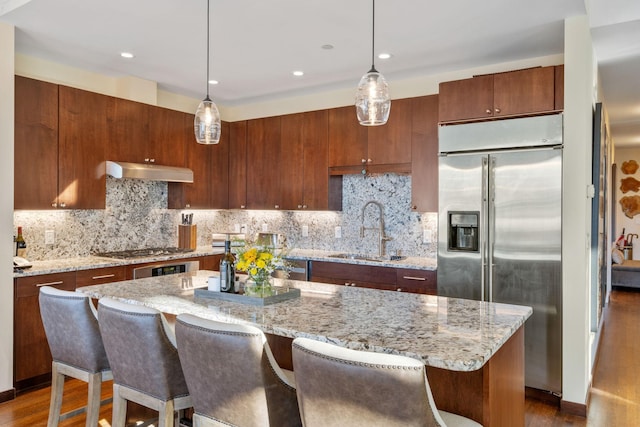 kitchen featuring a kitchen island, decorative light fixtures, sink, exhaust hood, and stainless steel appliances