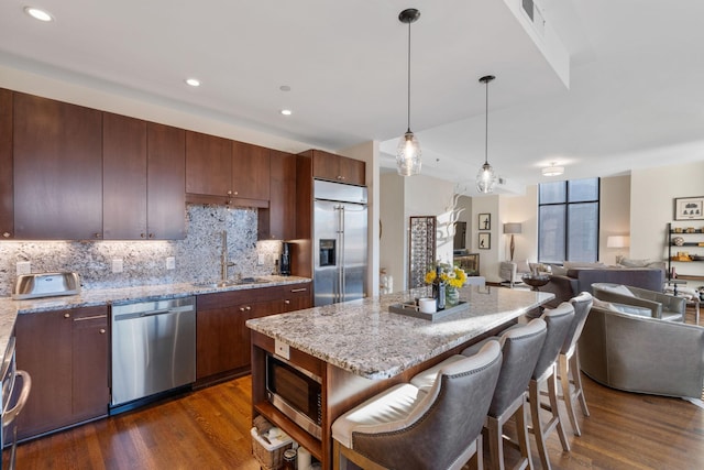 kitchen featuring dark wood-type flooring, sink, decorative light fixtures, a center island, and appliances with stainless steel finishes