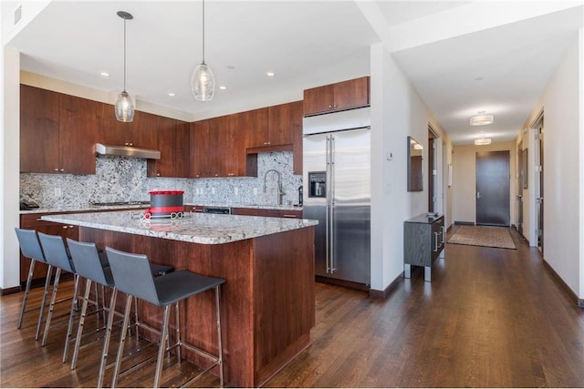 kitchen featuring sink, hanging light fixtures, a center island, decorative backsplash, and stainless steel built in fridge