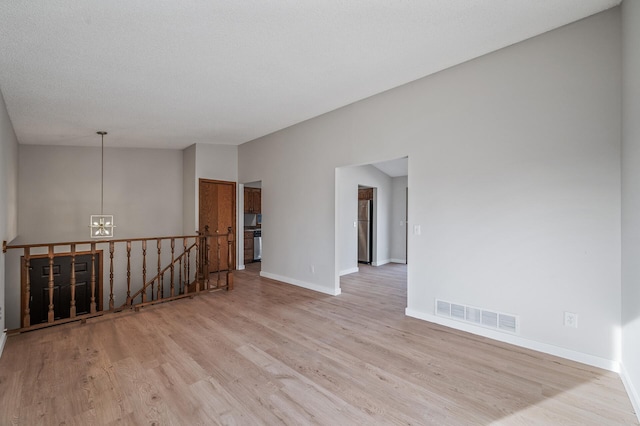 spare room featuring visible vents, an inviting chandelier, light wood finished floors, baseboards, and vaulted ceiling