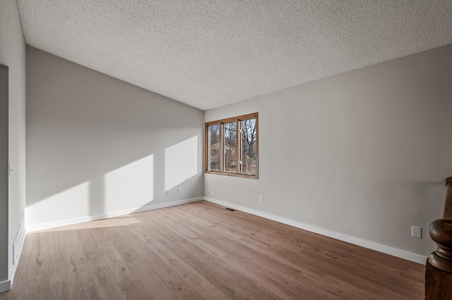 spare room with visible vents, a textured ceiling, baseboards, and wood finished floors