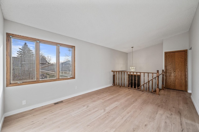 unfurnished room with visible vents, baseboards, vaulted ceiling, wood finished floors, and a textured ceiling