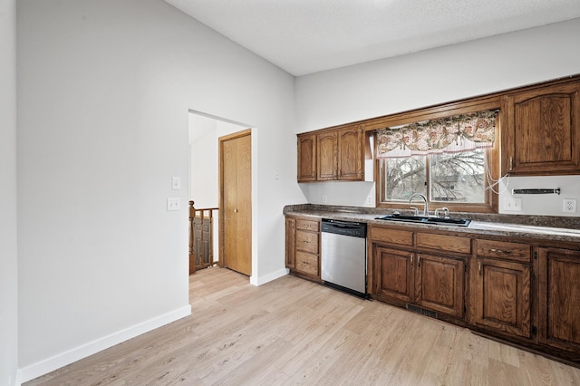 kitchen featuring baseboards, a sink, stainless steel dishwasher, dark countertops, and light wood-type flooring