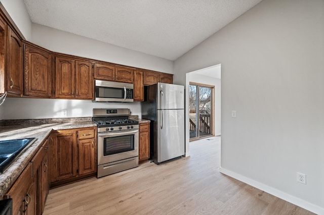 kitchen with light wood-style flooring, a textured ceiling, stainless steel appliances, and vaulted ceiling