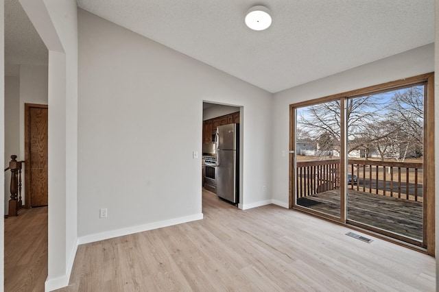 spare room featuring visible vents, baseboards, vaulted ceiling, light wood-style floors, and a textured ceiling