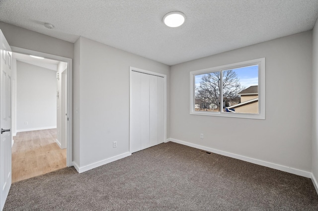 unfurnished bedroom featuring a closet, a textured ceiling, baseboards, and carpet floors