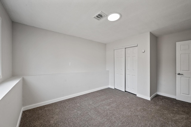 unfurnished bedroom with a closet, visible vents, dark carpet, and baseboards