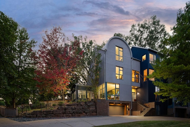 contemporary house with driveway, an attached garage, fence, and stucco siding