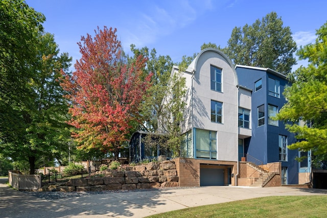 modern home with a garage, brick siding, fence, concrete driveway, and stucco siding