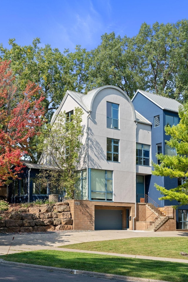 view of front of house with stucco siding, an attached garage, a front yard, metal roof, and driveway