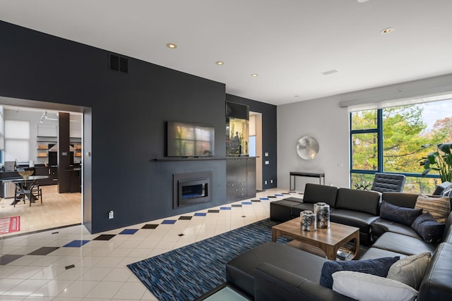 living room featuring light tile patterned flooring, a glass covered fireplace, visible vents, and recessed lighting