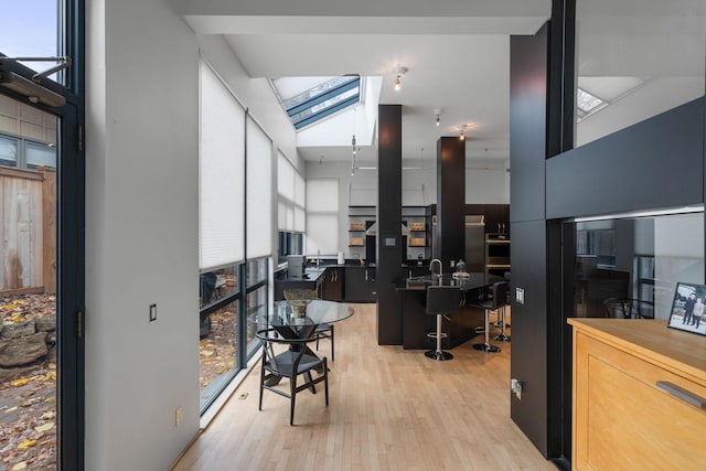 interior space featuring a towering ceiling, light wood-style flooring, a center island with sink, and a kitchen breakfast bar