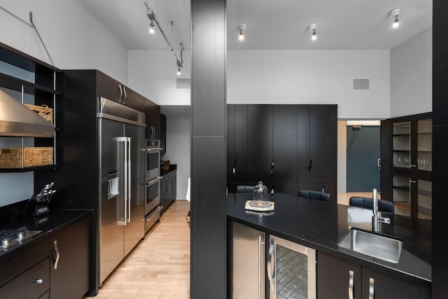 kitchen with wine cooler, visible vents, light wood-style flooring, a sink, and dark cabinetry