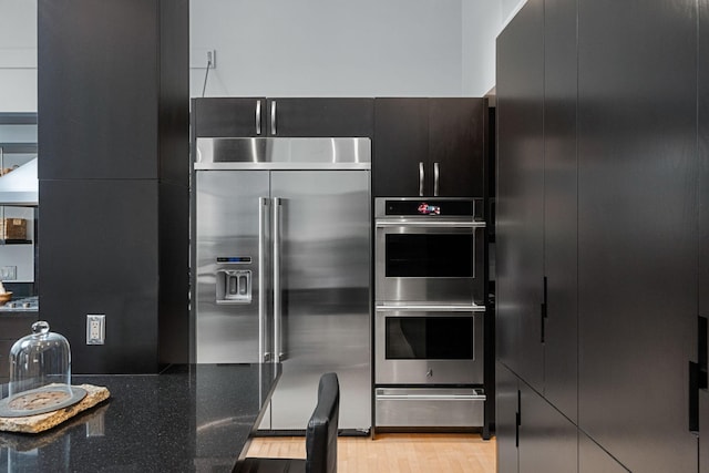 kitchen featuring a warming drawer, stainless steel appliances, light wood-style flooring, dark stone countertops, and modern cabinets