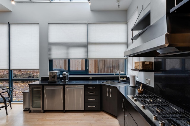 kitchen featuring beverage cooler, dark countertops, range hood, stainless steel gas stovetop, and a sink