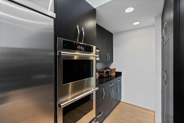 kitchen with light wood finished floors, dark countertops, dark cabinets, stainless steel appliances, and recessed lighting