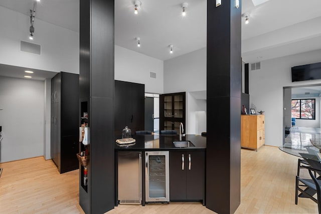 kitchen featuring beverage cooler, a towering ceiling, visible vents, dark cabinetry, and dark countertops