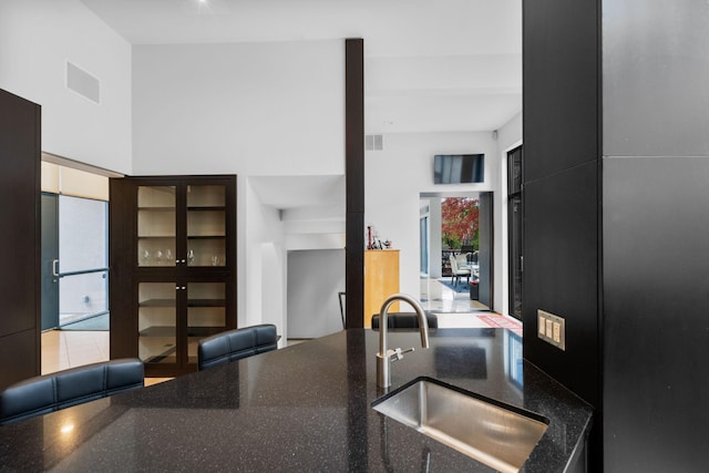 kitchen with a high ceiling, dark stone countertops, a sink, and visible vents