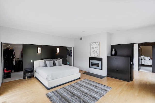 bedroom with a glass covered fireplace, visible vents, a spacious closet, and light wood finished floors