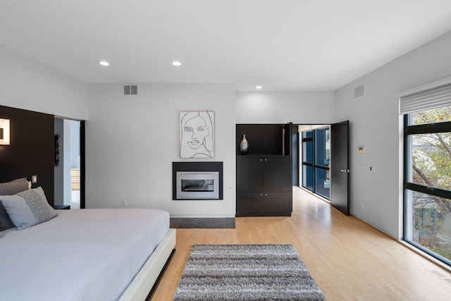 bedroom with light wood-type flooring, a glass covered fireplace, visible vents, and recessed lighting