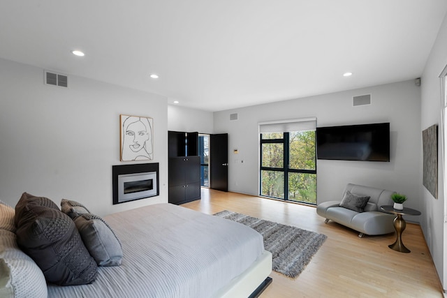 bedroom featuring light wood-style floors, a glass covered fireplace, visible vents, and recessed lighting