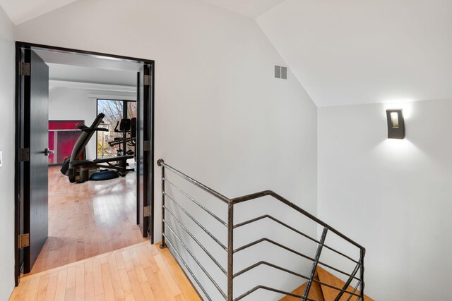 hall featuring wood-type flooring, visible vents, and vaulted ceiling