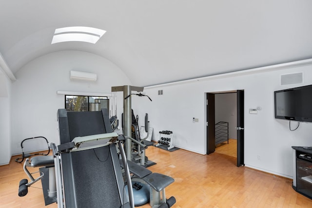 exercise room with light wood finished floors, lofted ceiling with skylight, a wall mounted AC, and baseboards