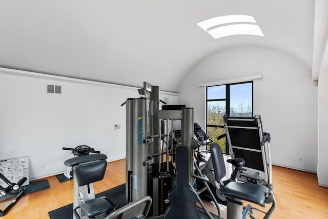 exercise room featuring lofted ceiling with skylight, visible vents, and wood finished floors