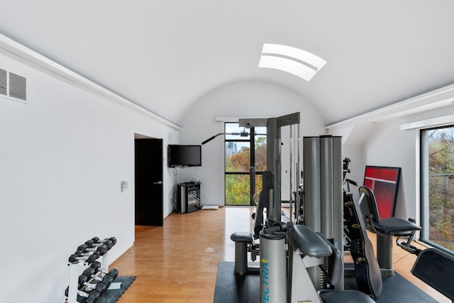 exercise area featuring vaulted ceiling with skylight, plenty of natural light, visible vents, and light wood-style floors