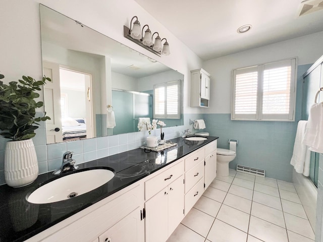 bathroom with toilet, tile walls, vanity, a shower with door, and tile patterned flooring