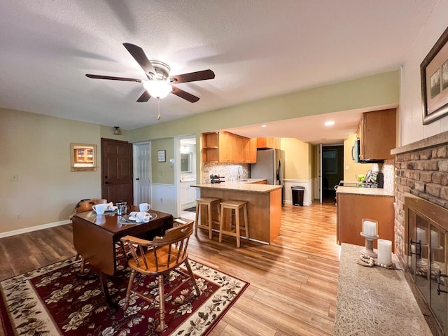 dining area featuring sink, a fireplace, ceiling fan, and light wood-type flooring