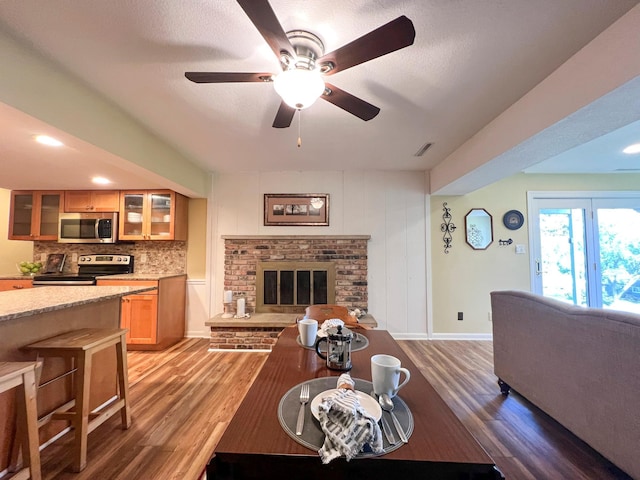 living room featuring a brick fireplace, dark wood-type flooring, and ceiling fan