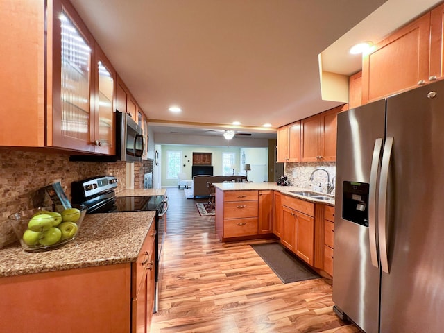 kitchen with sink, appliances with stainless steel finishes, tasteful backsplash, light hardwood / wood-style floors, and kitchen peninsula