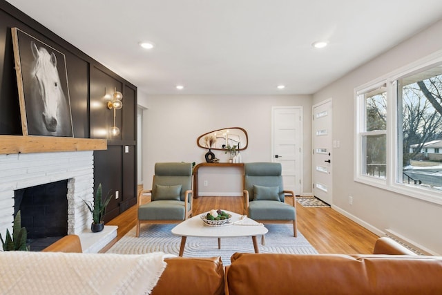 living room featuring a baseboard radiator, light hardwood / wood-style floors, and a brick fireplace