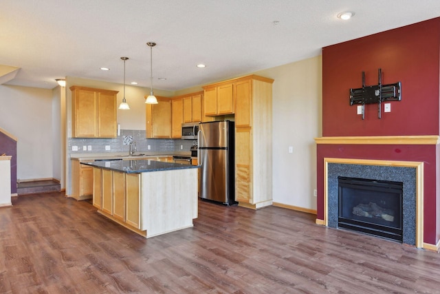 kitchen with sink, appliances with stainless steel finishes, hanging light fixtures, a kitchen island, and light brown cabinetry