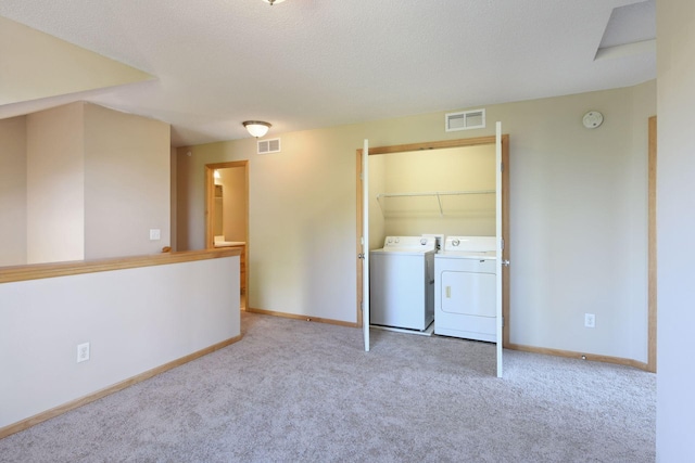 laundry area with light colored carpet, washer and dryer, and a textured ceiling