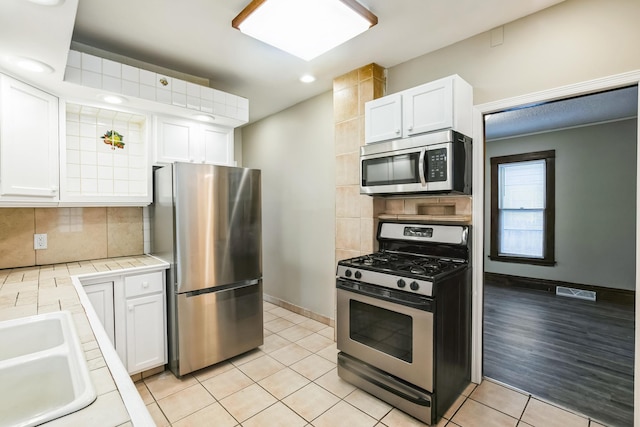 kitchen with stainless steel appliances, white cabinetry, tasteful backsplash, and tile counters